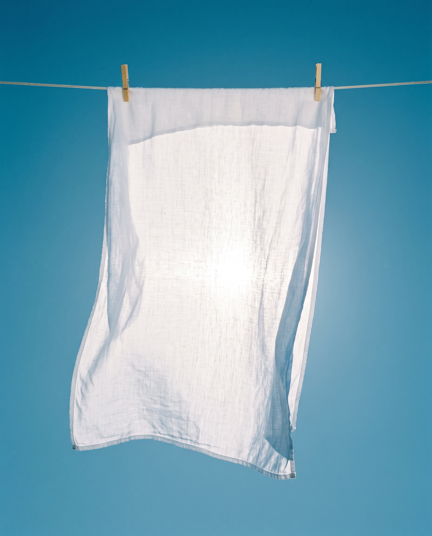 A white linen sheet on the line against a deep blue sky, sun glowing through the weave.
